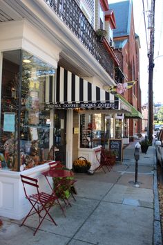 an empty sidewalk in front of a coffee shop with chairs and tables on the side