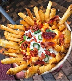 a hand holding a bowl filled with french fries covered in cheese and bacon