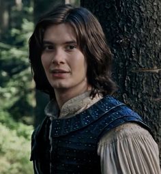 the young man is standing next to a tree