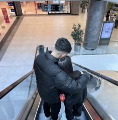 a man and woman riding an escalator in a shopping center with their arms around each other