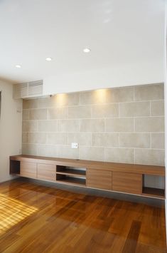 an empty living room with wood floors and white brick wall behind the entertainment center that's built into the wall