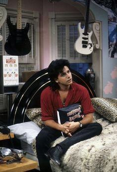 a man sitting on top of a bed in a room with guitars hanging from the ceiling