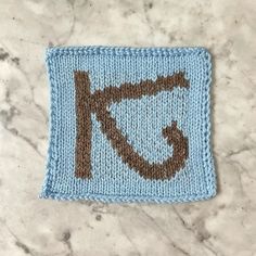 a knitted square with the letter k in brown and blue on top of it