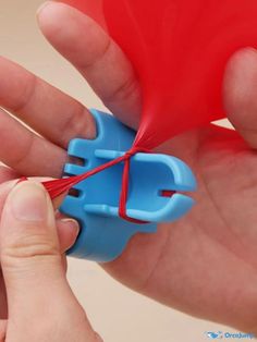 a hand holding a blue and red object in it's left hand with string attached to it