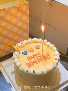 a birthday cake with a lit candle on it sitting in front of a gift box