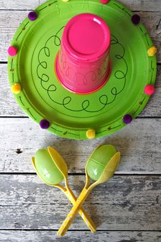 a green plate with two spoons and a pink cup on it next to yellow plastic utensils