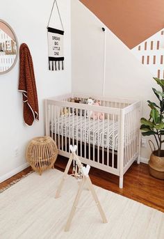 a baby's room with a white crib, potted plant and mirror on the wall