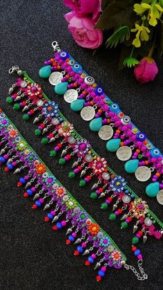 three bracelets with different colored beads and charms on each strand, sitting next to flowers