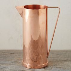 a copper colored pitcher sitting on top of a wooden table