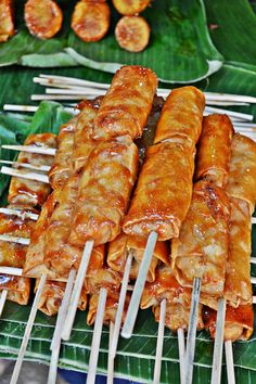 several skewers of food sitting on top of a green leaf covered tray next to other foods