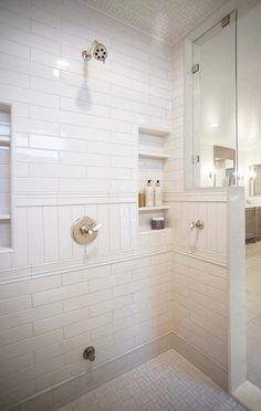 a white tiled bathroom with glass shower doors and shelves on the wall, along with a walk in shower