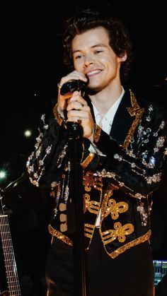 a man that is standing in front of a microphone and wearing a suit with gold sequins on it