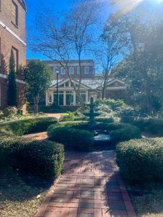 a brick walkway leads to a large house with trees and bushes in the foreground