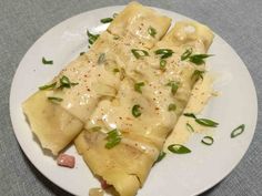 a white plate topped with ravioli covered in gravy and garnished with green onions