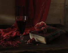 a glass of wine sitting on top of a table next to a book and pomegranate