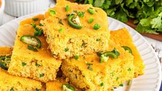 several pieces of cornbread on a white plate with green onions and jalapenos