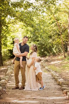 a man and woman holding two children while standing on a path in the woods