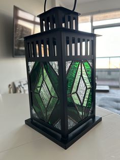 a green stained glass lantern sitting on top of a white table next to a window