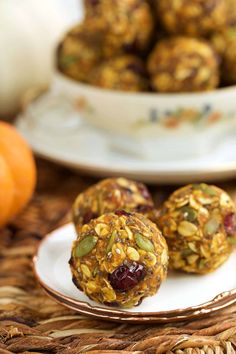 three balls of granola energy bites on a plate next to a bowl of pumpkins