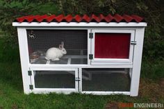 a white rabbit sitting inside of a cage on top of green grass next to trees