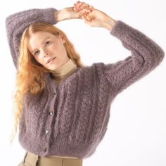 a woman with red hair wearing a purple sweater and khaki pants is posing for the camera