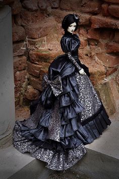 a mannequin wearing a black and silver dress in front of a stone wall