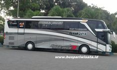 a silver and black bus is parked on the side of the road in front of some trees