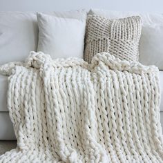 a white couch with a blanket on top of it next to some pillows and blankets