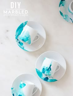 two cups and saucers with blue swirled paint on them, sitting on white plates