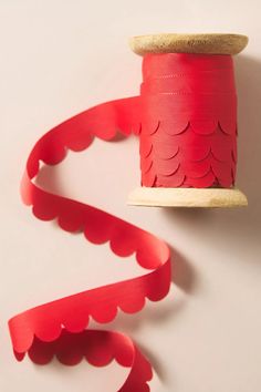 a spool of red paper next to a roll of red ribbon on a white surface