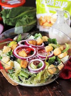 a salad with croutons, onions and lettuce in it on a wooden table