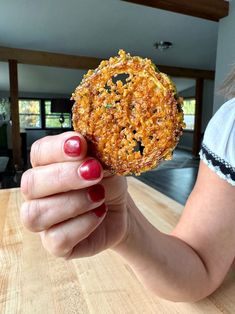 a woman holding up a fried pastry on top of a wooden table