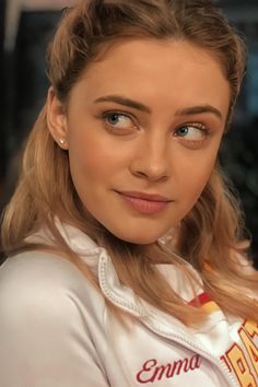 a young woman with long hair wearing a white shirt and smiling at the camera while looking into the camera