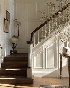 the stairs are lined with white flowers and framed pictures on the wall, along with vases