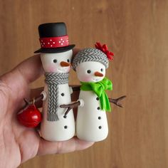 two snowmen are standing next to each other with a bell on their head and one is holding a red apple