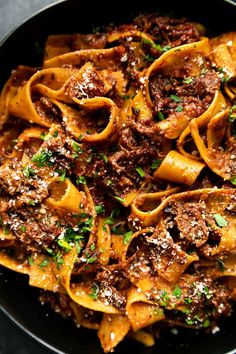 pasta with meat sauce and parsley in a black bowl on top of a table