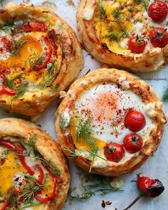 four small pizzas with different toppings are on a table together, one has an egg and the other has cherry tomatoes