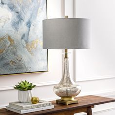 a table with a lamp, books and a painting on the wall in the background