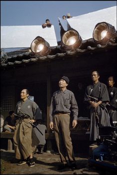 three men standing in front of a building with two lights on their heads and one man holding a camera