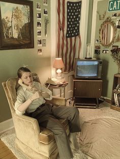 a person sitting in a chair with a cat on his lap and an american flag behind them