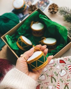 a person holding a small christmas ornament in front of a box filled with candles