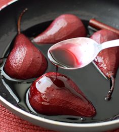 some pears are in a pan with syrup on them and the spoon is being drizzled over them