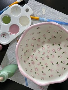 a pink flowered bowl sitting on top of a table next to paintbrushes