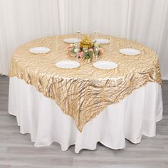 a gold table cloth with white plates and flowers on it is set up in front of a curtain