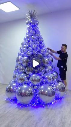 a man is decorating a christmas tree with blue lights and silver baubles