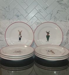 four white plates with red trim decorated with deer and cactus designs on them, sitting in front of a tiled wall