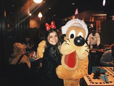 a woman standing next to a person in a goofy mouse costume at a table with other people