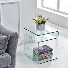 a glass table with books on it in front of a couch and chair next to a window