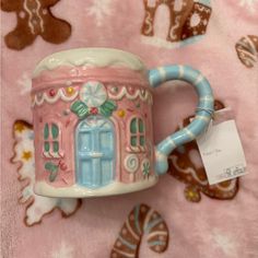 a pink and blue coffee mug with a house on it sitting on a pink blanket