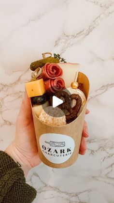 a person holding up a cup filled with different types of food on top of a marble counter